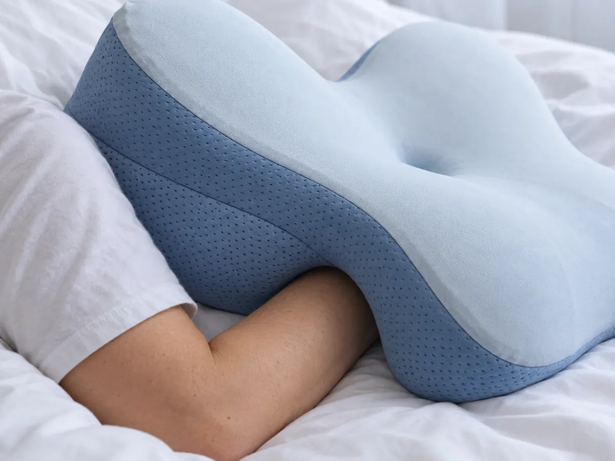 A sleeper's arm tucked under one of the pillow's curved side cutouts